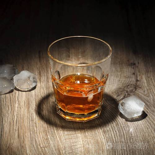 木制桌子上有冰块的酒精饮料黑底杯威士忌